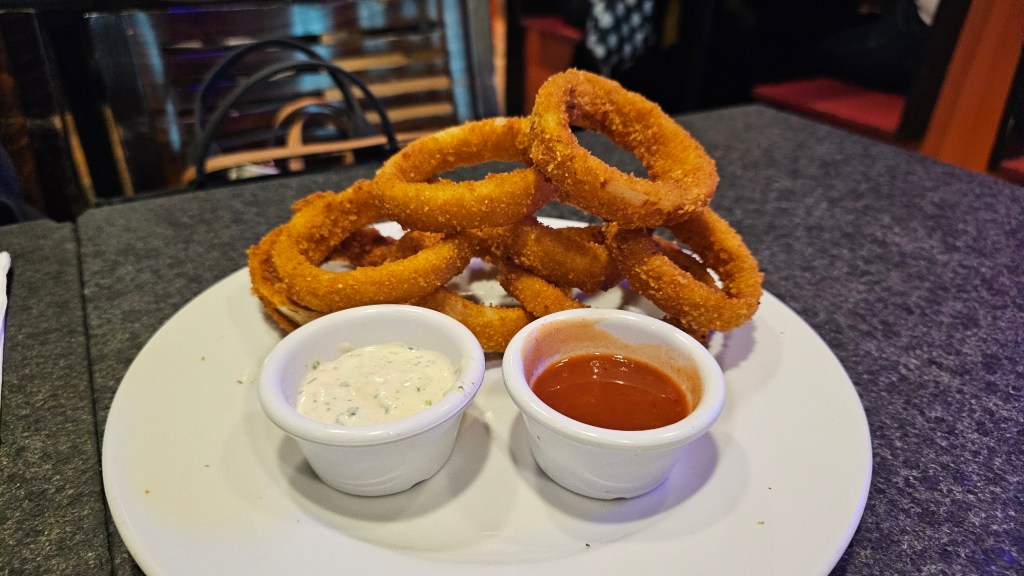 Aros de cebolla de Chazz en un plato blanco, acompañado de dos diferentes salsas.