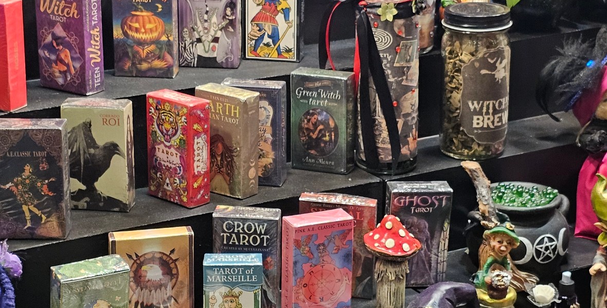 Un puesto que exhibe diferentes diseños de tarot, gnomos, botellas aromáticas y calderos.