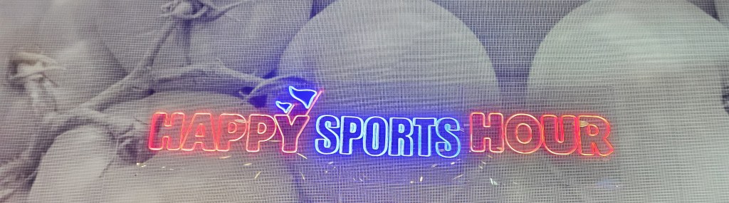 Letrero de chazz iluminado en el muro del restaurante que dice Happy Sports Hour